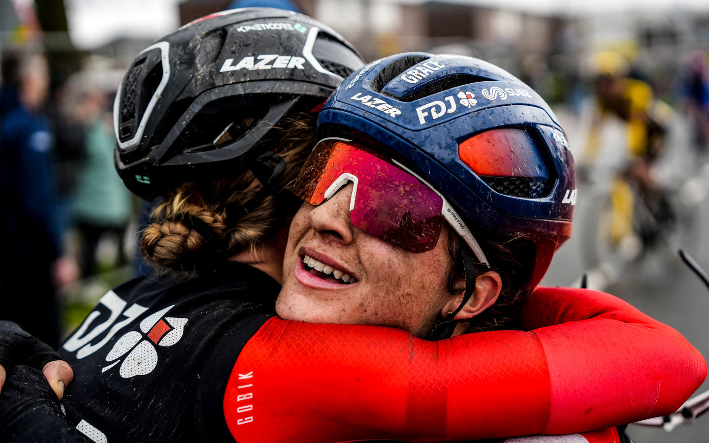 Due ciclisti della squadra FDJ Suez si abbracciano alla fine dell'Amstel Gold Race. I loro volti coperti di fango, i loro kit e il sorriso sul volto di uno di loro mostrano la durezza della corsa e la soddisfazione del ciclista che riesce a vincerla.