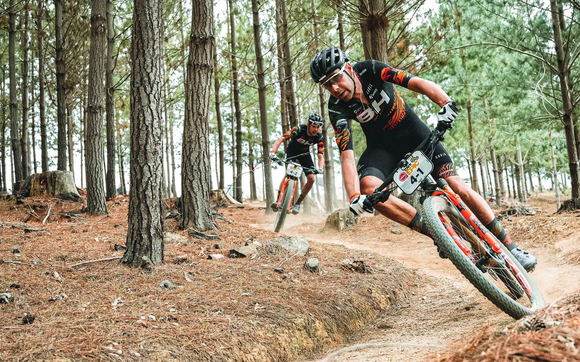 Rodríguez und Valero, Fahrer des BH Coloma-Teams, durchqueren ein Waldstück des Rennens. Sie tragen die Gobik Trikot der Sonderschule Cape Epic und an ihren Gesten auf dem Rad kann man die technische Komplexität des Rennens erkennen. 