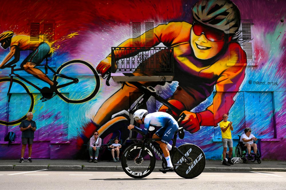 Nelson Oliveira in the time trial of stage 16 of the Tour, behind a very colorful cycling-themed mural, painted with graffiti on the wall.