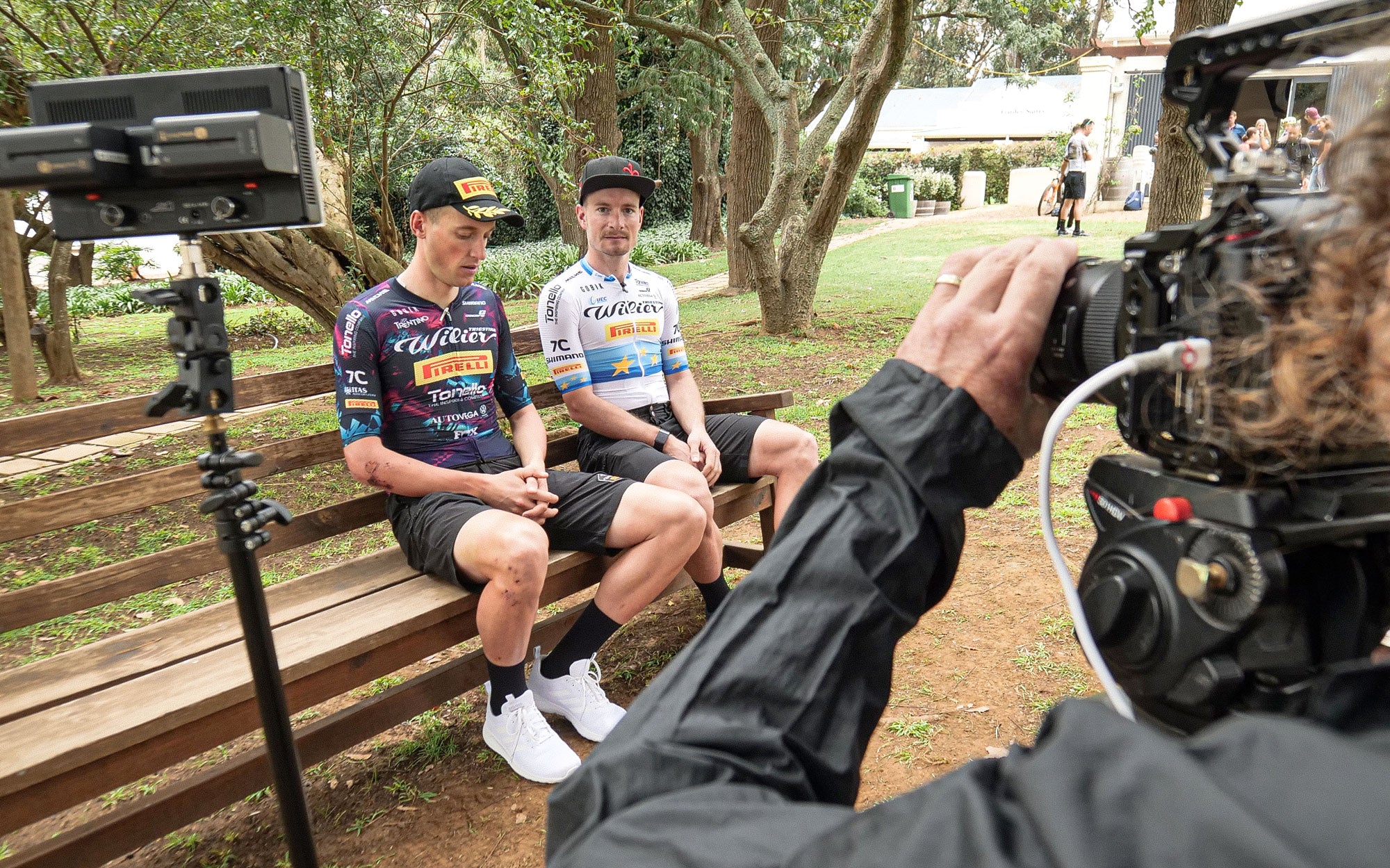 Two riders from the team Wilier Pirelli in front of a video camera while sitting on a bench, both wearing the jersey that Gobik designed for their participation in Cape Epic.