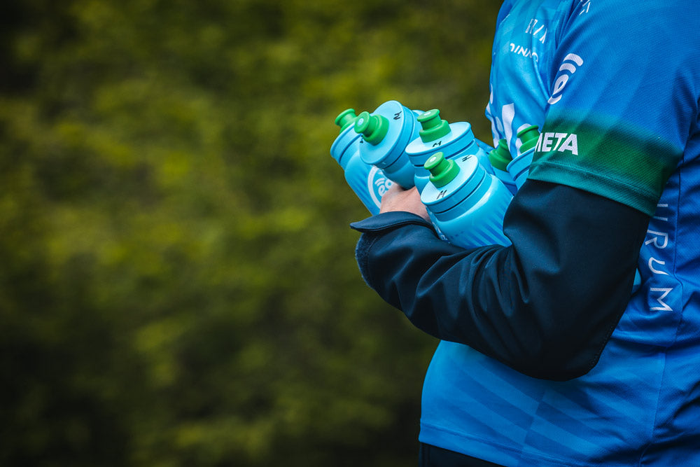 Un miembro del equipo de comunicación del Eolo Kometa porta cinco bidones en sus brazos para repartir a los aficionados.