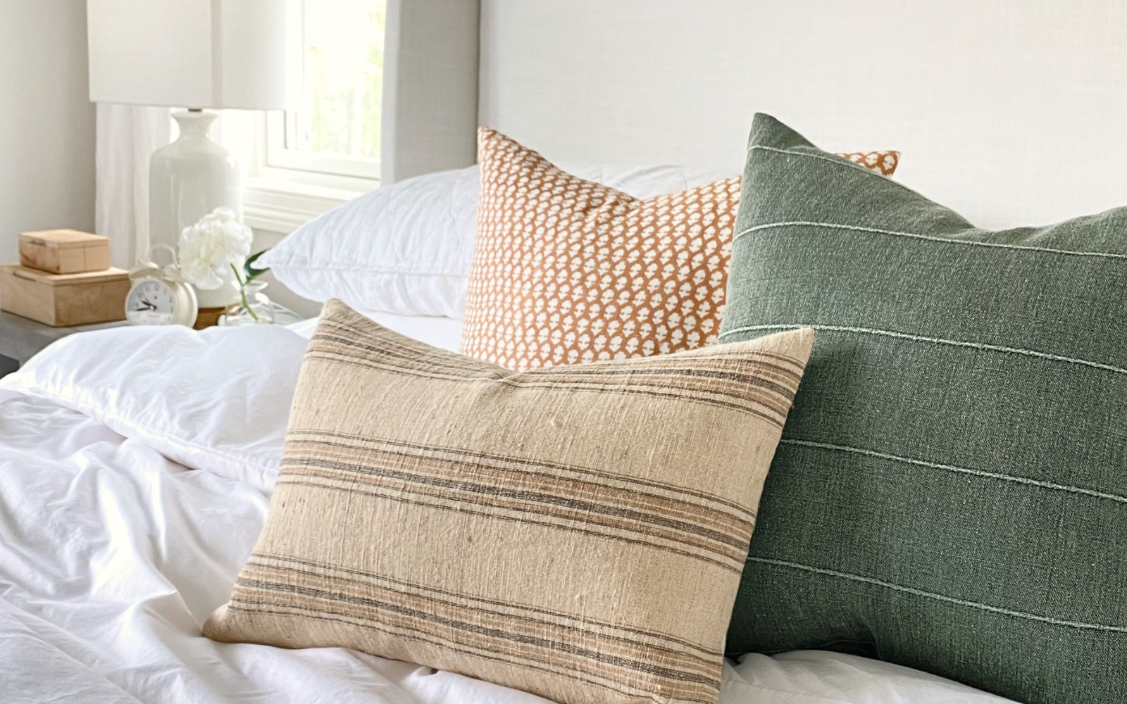 Cream, green, and neutral colored throw pillow arrangement on top of a white bed