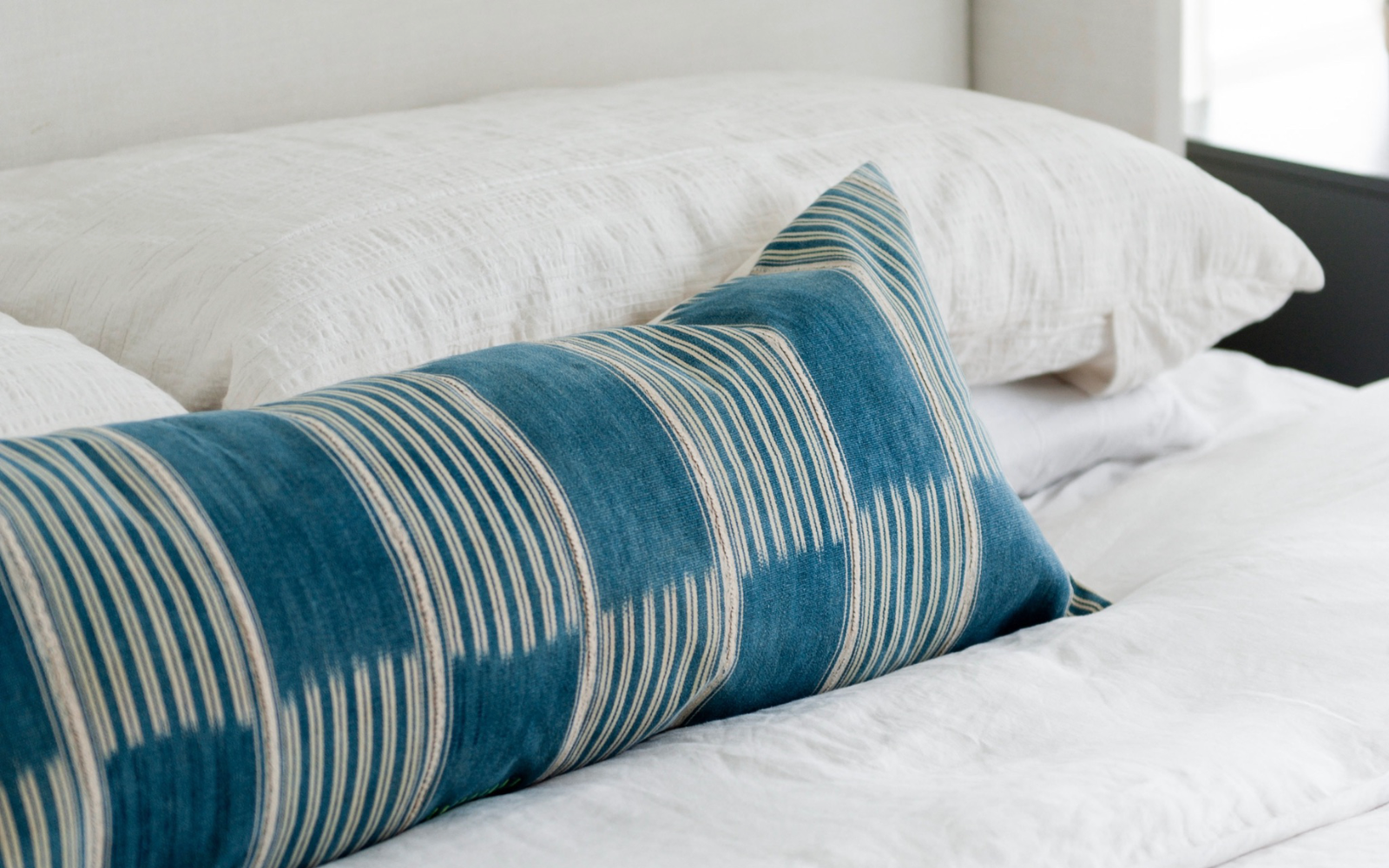 One large blue lumbar pillow on a white bed to show a minimalist style