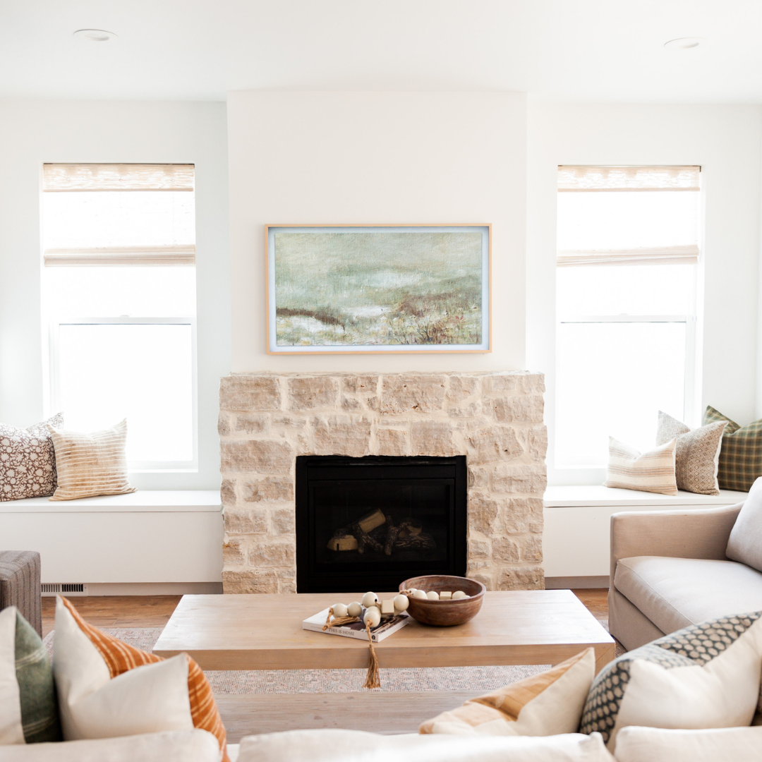 living room centered around fireplace with two sofas full of colorful accent pillows. Also featured are two window seating areas with throw pillows to brighten the space