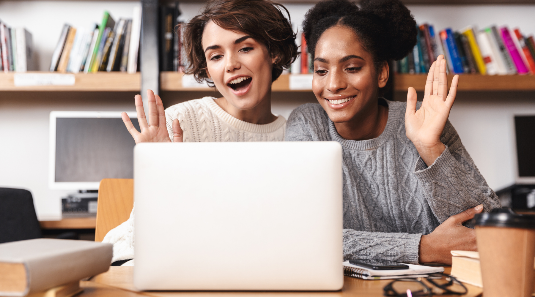 Two young students waving and smiling in front of laptop. 