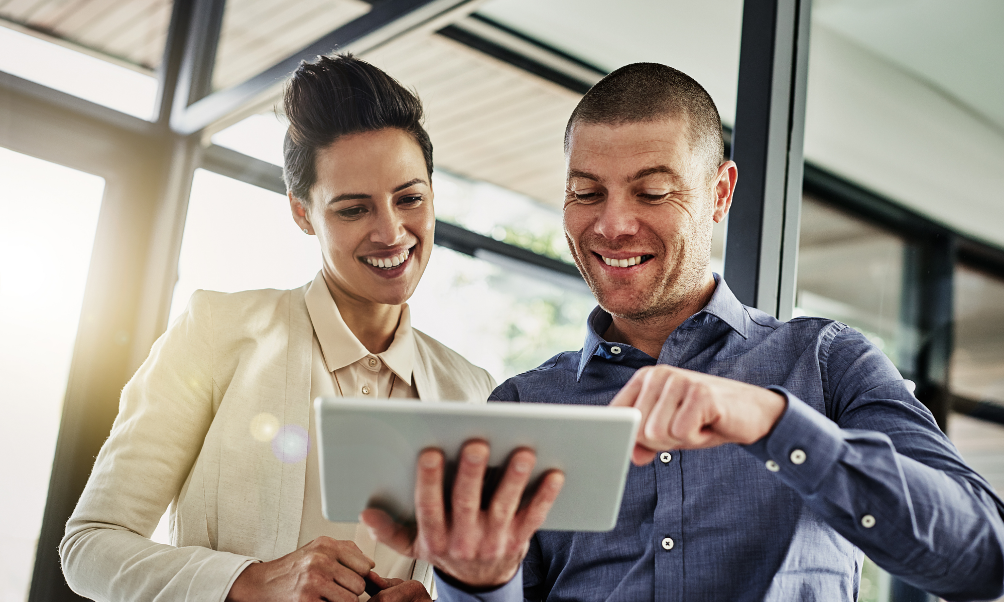 Two smiling coworkers looking at tablet together in an office. 