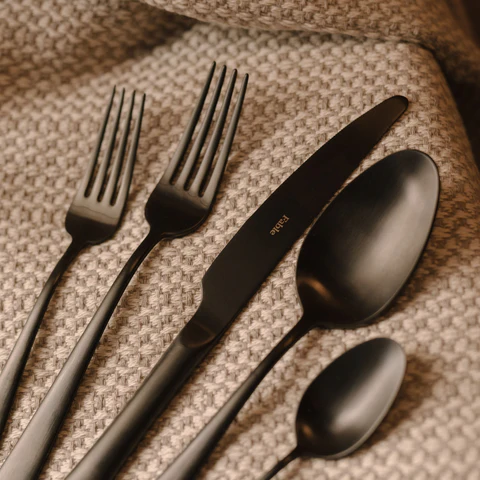 Serving utensils and flatware on a woven surface. 