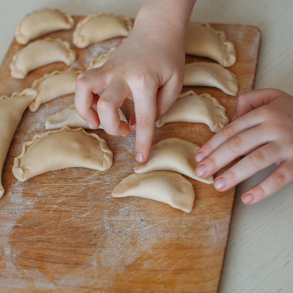 Hands shaping perogies on a wooden surface.