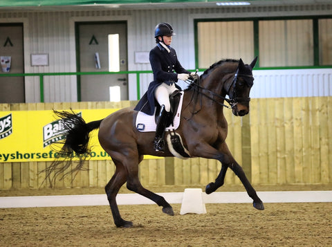 Natasha Rumble riding a brown horse around an indoor arena