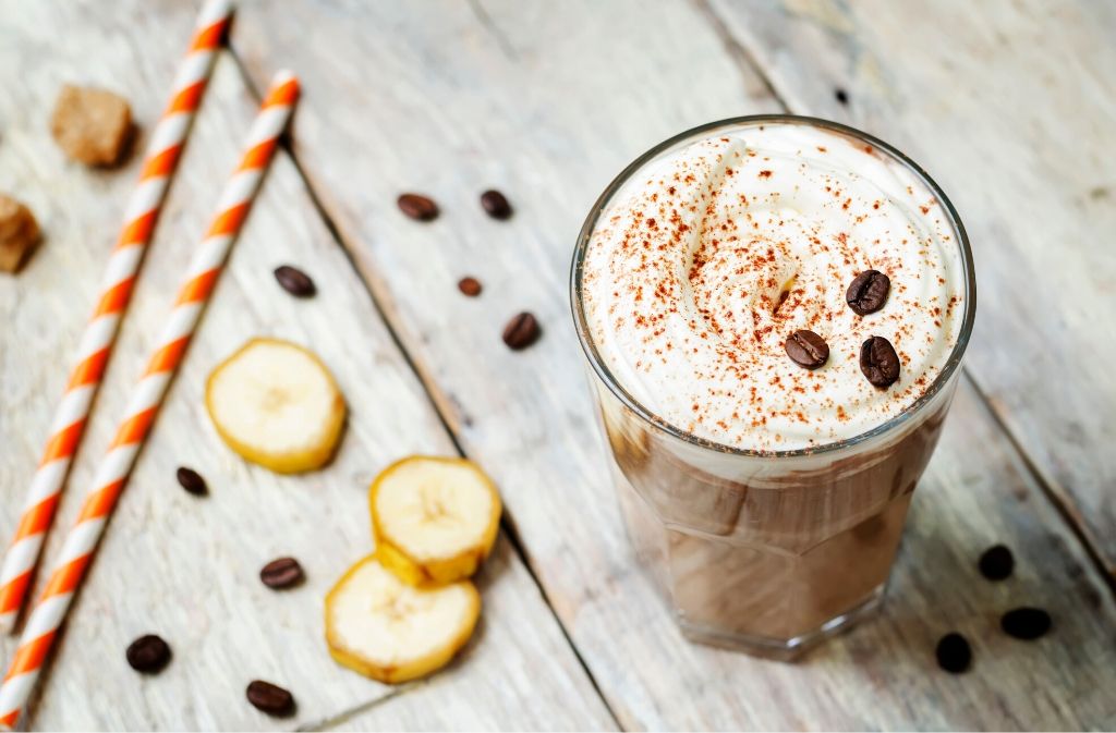 glass cup of adaptogen mushroom smoothie on a wood surface beside slices of banana and two striped straws