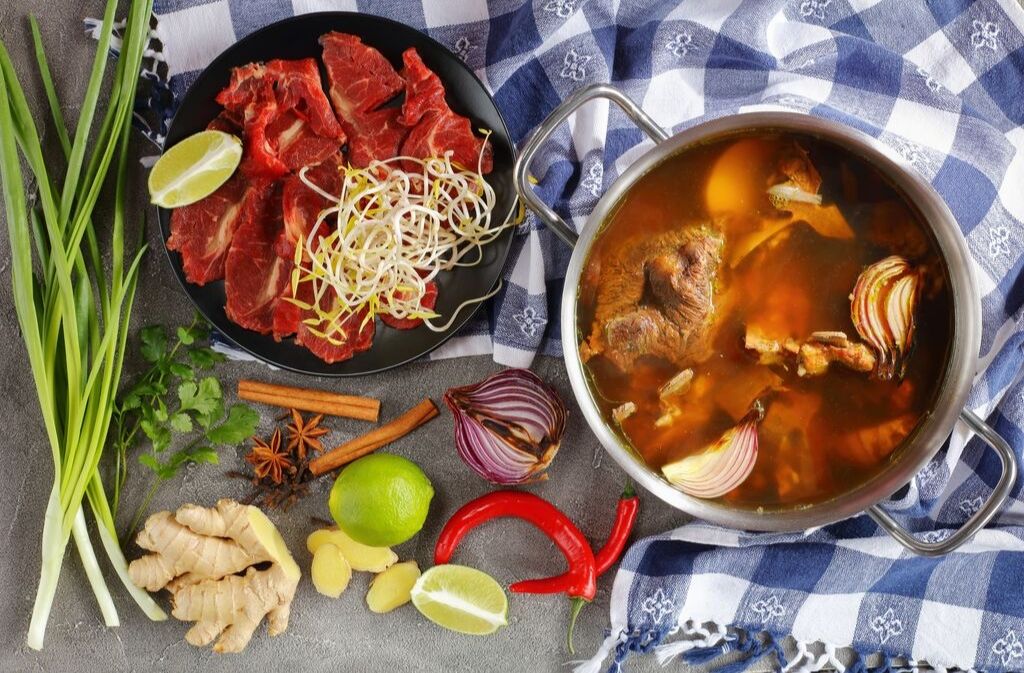 a pot of bone broth stew beside a plate with beef and assorted vegetables