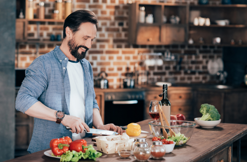bearded man smiling while chopping vegetables in a modern kitchen with a brick wall