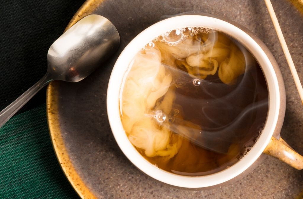 mug of creamy keto tea on a brown saucer beside a metal spoon