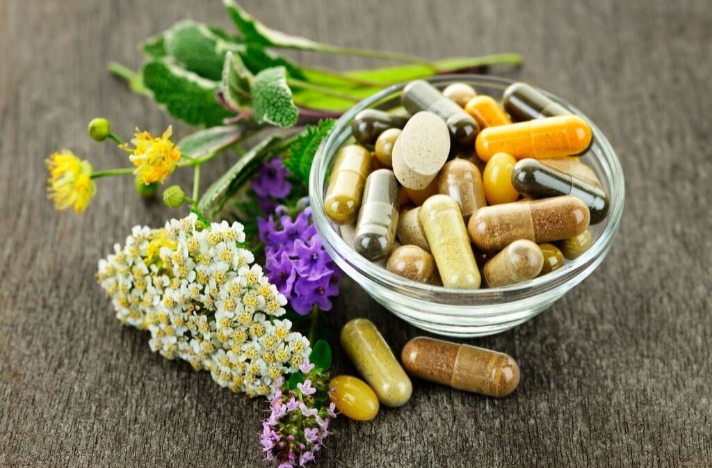 a bowl of vitamins next to medicinal plants and herbs