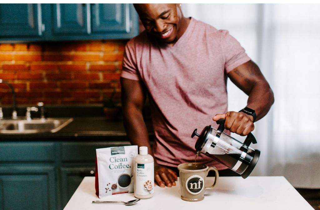 smiling man pouring a French press of coffee into a handmade natural force mug