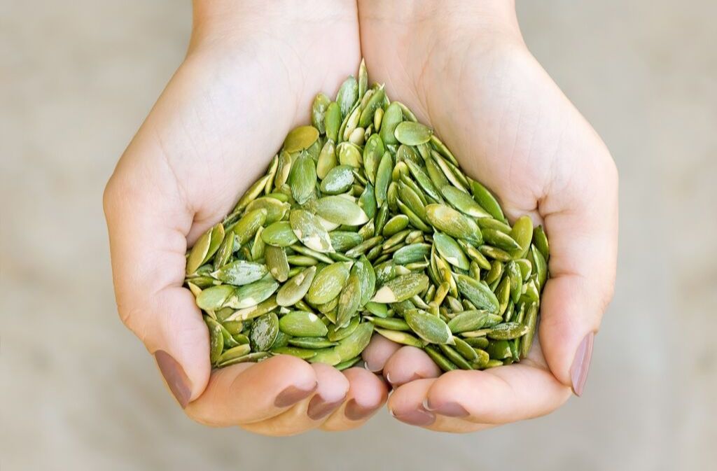 hands holding a heart shaped pile of pumpkin seeds a grain free vegan protein source