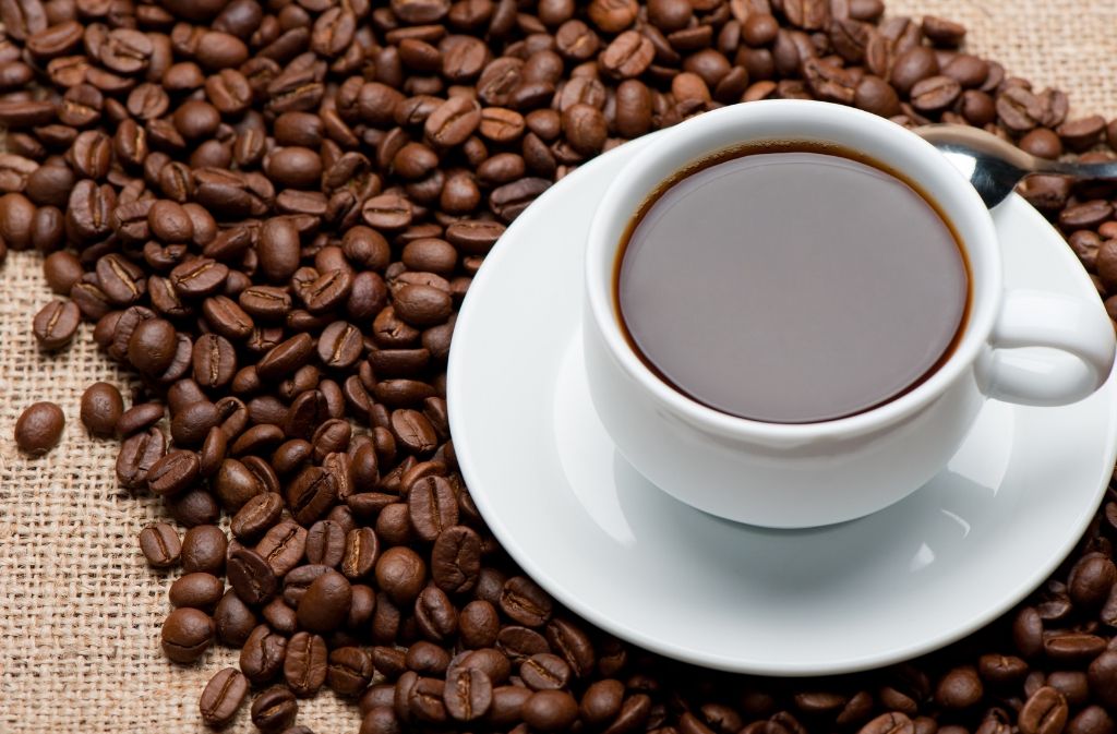 homemade cold brew coffee served hot in a white mug and saucer surrounded by coffee beans