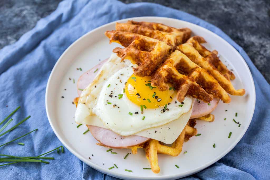 keto chaffle breakfast sandwich with sunny side up egg and deli meat on a blue cloth