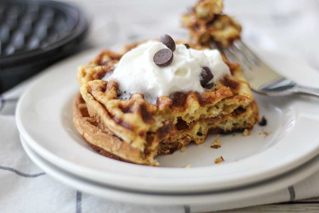 chocolate chip Keto chaffles topped with whipped cream and chocolate chips on a white plate 
