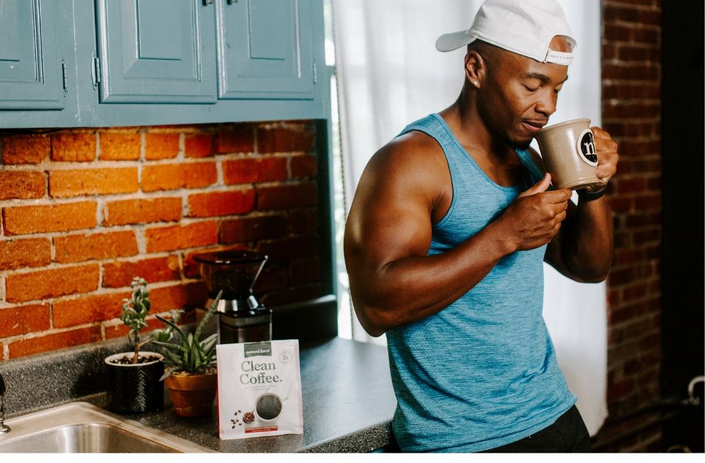 athletic man leaning against a counter smiling as he smells a mug of natural force clean coffee