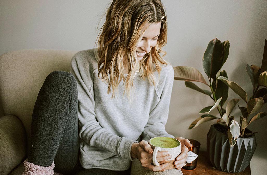 athletic woman smiling looking down at a mug of keto matcha latte in her hands