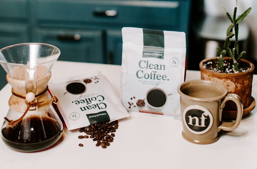 a chemex of coffee beside two bags of mold and mycotoxin free natural force clean coffee and a hand crafted natural force mug