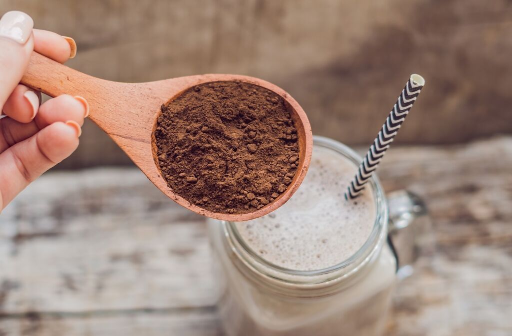 wooden spoon holding the best plant based protein powder over a protein smoothie