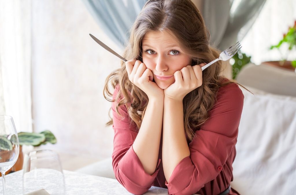 a pretty woman holding a knife and fork with her head in her hands looking sad