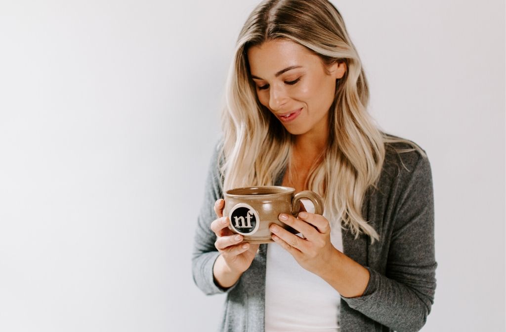 pretty blond woman smiling down at handcrafted natural force mug filled with keto coffee that she's holding in her hands