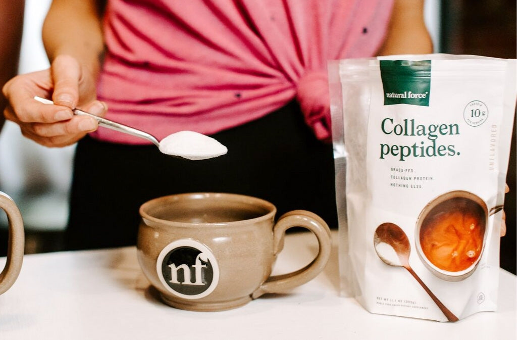 woman in pink shirt holding a spoonful of grass fed collagen peptides above a natural force ceramic stoneware mug