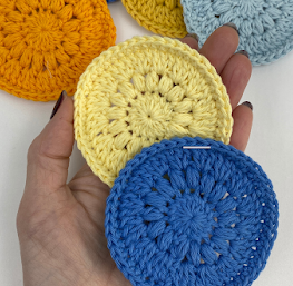 crochet makeup remover pads pattern - blue, yellow, orange, gold and light blue reusable face pads against a white background