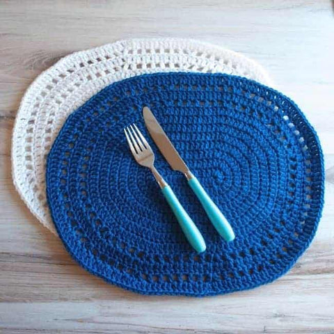 crochet placemats free patterns - blue and white oval placemats plus knife and fork shown against a wooden background