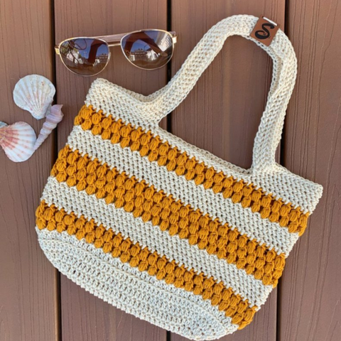 crochet beach bag pattern - cream and gold crocheted beach bag with sunglasses and shells against a wooden background