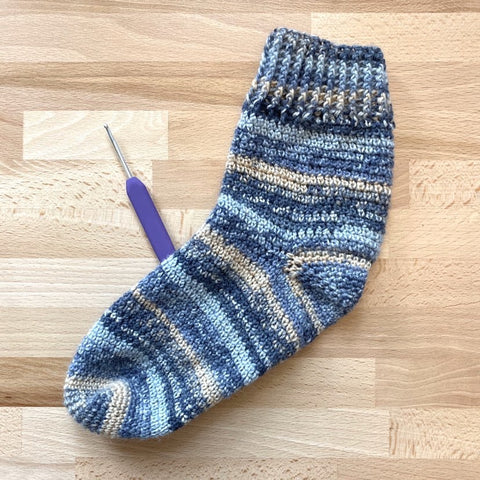crochet sock pattern toe up - blue variegated crochet sock shown against a light wooden background