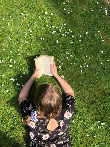 Woman laying in green grass reading a book with a daisy print hair scrunchie in hair