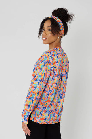 woman in bright multicoloured retro print button down shirt and twist knot headband