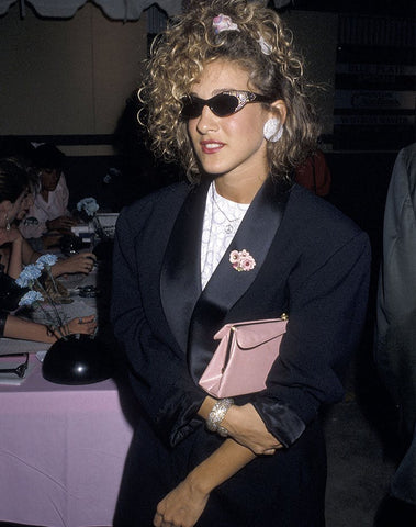 Sarah Jessica Parker in 90's scrunchie with black jewelled sunglasses and black satin blazer holding a light pink purse