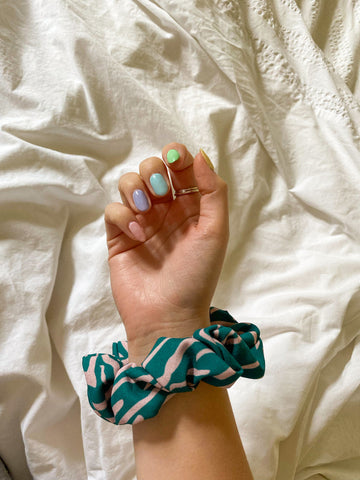 hand with painted pastel nails and a green and pink animal print zebra hair scrunchie around wrist