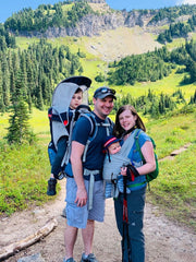A family hiking at Mt. Rainier National Park with two young boys in baby carriers 