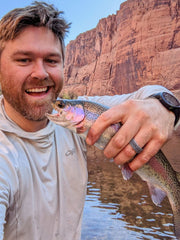 A man holding a trout next to a river
