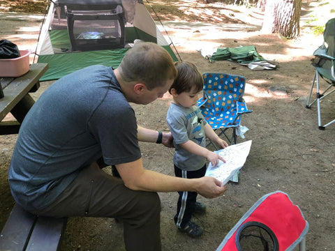 A man looking over a map to a campground with a little boy in front of a tent