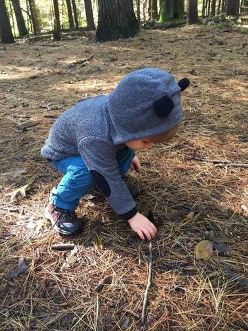 A young child picking up sticks wearing hiking boots in a wooded area