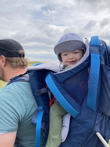 A man wearing a smiling baby in a Kelty framed hiking pack while hiking in grasslands