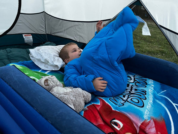 A young boy wearing a Morrison Outdoors Big Mo 40 sleeping bag in a tent