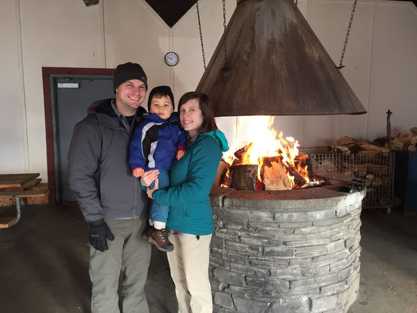 A couple holding a small child in front of a large fire pit inside the warming hut at Saratoga Spa State Park
