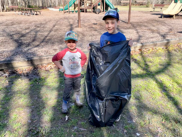 Two little boys smiling while wearing gloves and carrying a trash bag after cleaning up a trail