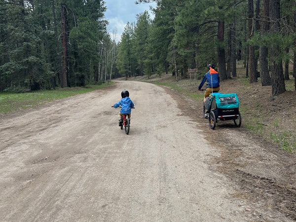 A man on a bike hauling a Burley Trailer next to a child riding a bike on a wide trail