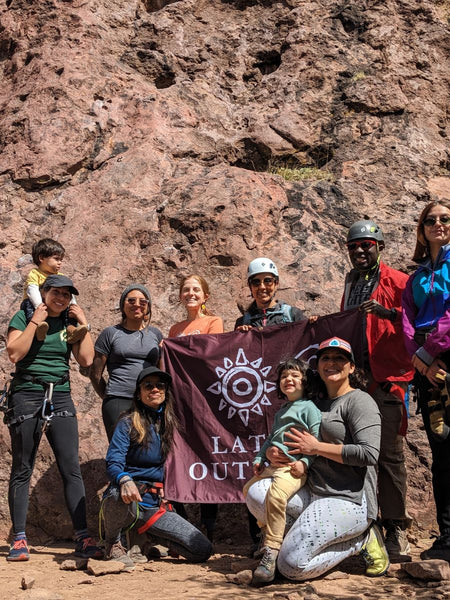 A group of people smiling in front of a rock formation while holding a banner for the Latino Outdoors Organization