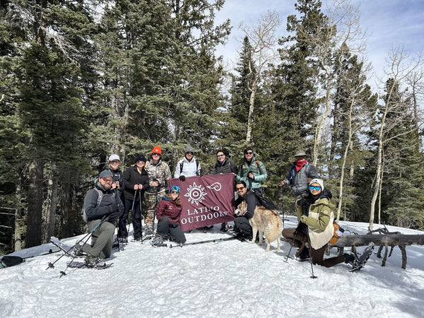 A group of people snowshoeing on a snowy hill and holding a banner for the Latino Outdoors Organization