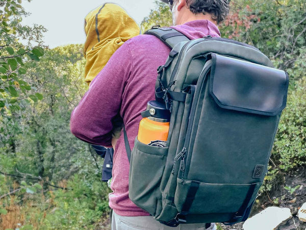 A man holding a child while hiking and wearing a Milk X Whiskey Adventure Proof Diaper Backpack